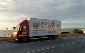 Camion di Kasali Traslochi parcheggiato di fronte al mare, pronto per un trasloco internazionale.